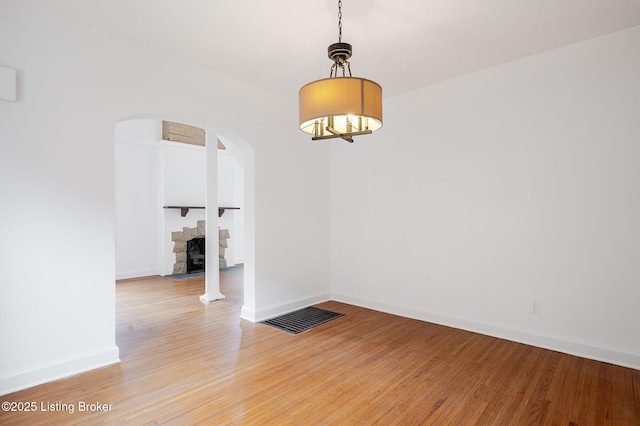 spare room featuring light wood-style floors, a fireplace, baseboards, and arched walkways