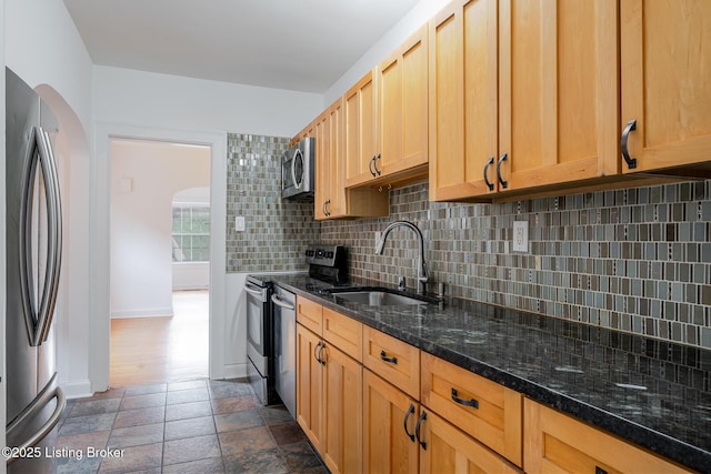 kitchen featuring stone tile flooring, backsplash, appliances with stainless steel finishes, a sink, and dark stone countertops