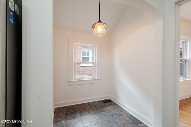 empty room with baseboards, visible vents, arched walkways, and stone finish flooring