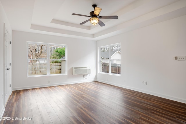 spare room featuring baseboards, a ceiling fan, a wall unit AC, wood finished floors, and a tray ceiling