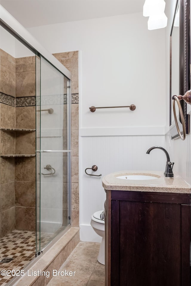 full bathroom featuring a wainscoted wall, a stall shower, vanity, and toilet