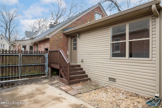 view of side of property with crawl space, a gate, fence, and brick siding