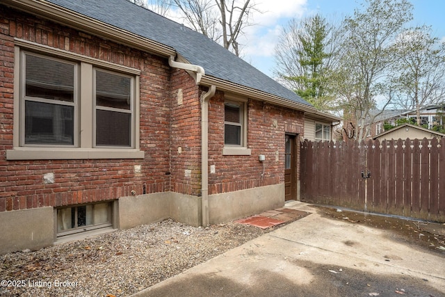 view of side of home featuring a shingled roof, fence, and brick siding