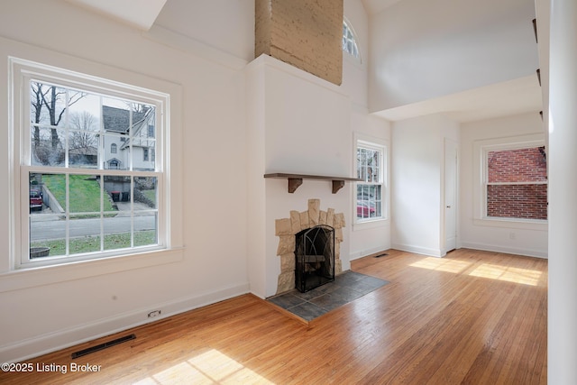 unfurnished living room featuring a wealth of natural light, visible vents, a stone fireplace, and wood finished floors