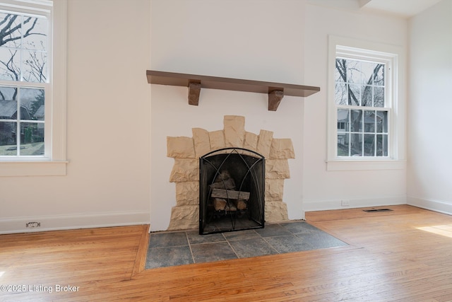 room details with a fireplace with flush hearth, visible vents, baseboards, and wood finished floors