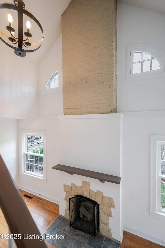 unfurnished living room with high vaulted ceiling, a stone fireplace, wood finished floors, and visible vents