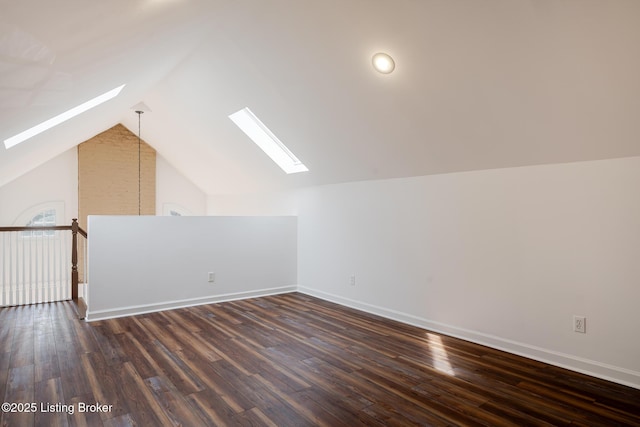 additional living space featuring vaulted ceiling with skylight, baseboards, and wood finished floors