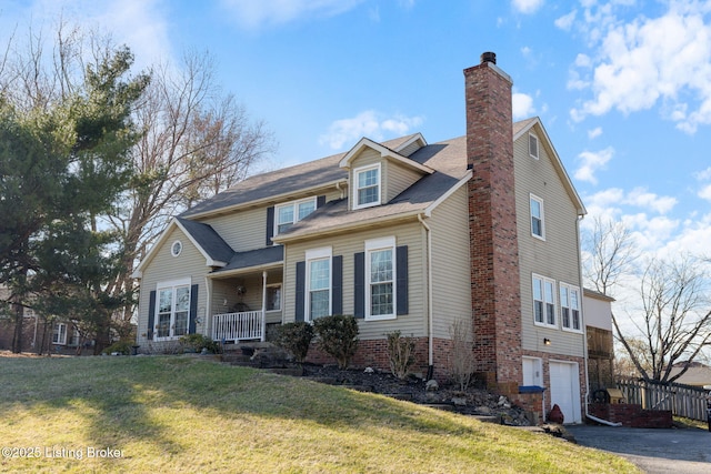 view of front of property with an attached garage, covered porch, driveway, a chimney, and a front yard