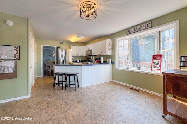 kitchen featuring stainless steel appliances, visible vents, white cabinets, a sink, and a peninsula