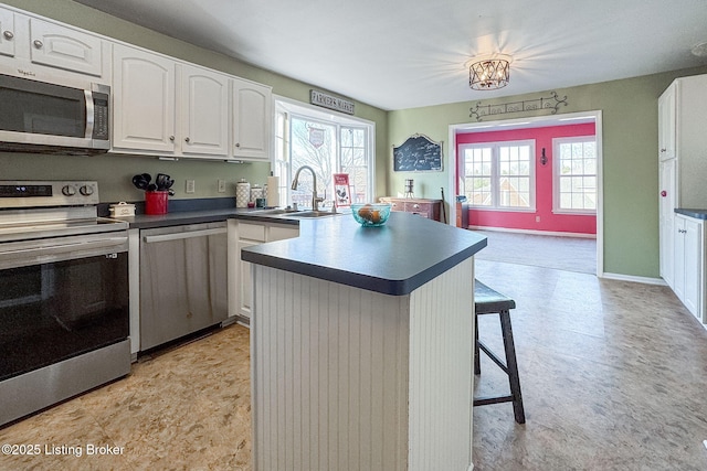 kitchen with a breakfast bar, a sink, white cabinetry, appliances with stainless steel finishes, and dark countertops