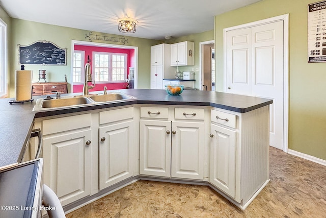 kitchen with dark countertops, baseboards, white cabinets, and a sink