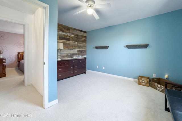 bedroom featuring ceiling fan, an accent wall, baseboards, and light colored carpet