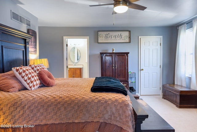 carpeted bedroom featuring ensuite bath, visible vents, and a ceiling fan