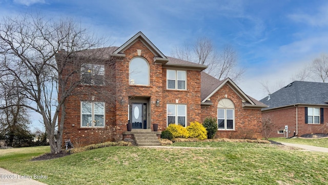 colonial inspired home featuring roof with shingles, brick siding, and a front lawn