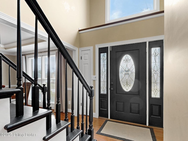 entrance foyer with light wood-type flooring, crown molding, a towering ceiling, and stairs