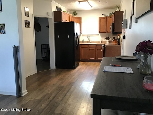 kitchen with brown cabinetry, stainless steel microwave, wood finished floors, black refrigerator with ice dispenser, and a sink