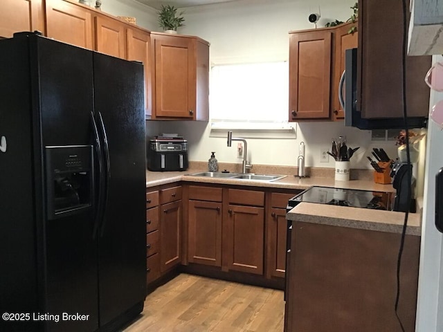 kitchen with light wood-style flooring, a sink, black fridge with ice dispenser, light countertops, and brown cabinetry