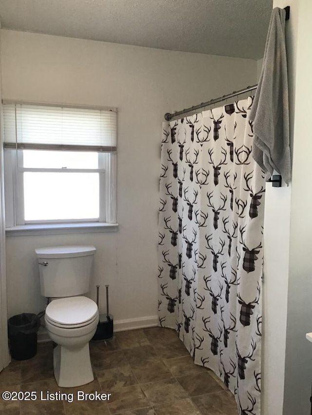 full bathroom featuring toilet, baseboards, a textured ceiling, and a shower with shower curtain