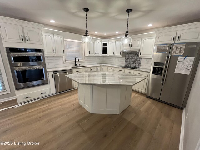 kitchen with light wood finished floors, stainless steel appliances, decorative backsplash, white cabinets, and a sink