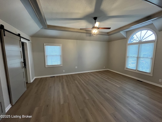 unfurnished bedroom with a barn door, baseboards, and dark wood finished floors