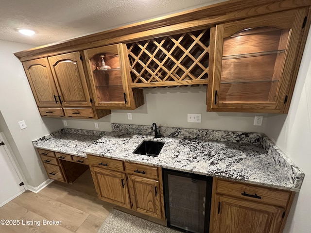 kitchen with light stone countertops, beverage cooler, baseboards, and a sink