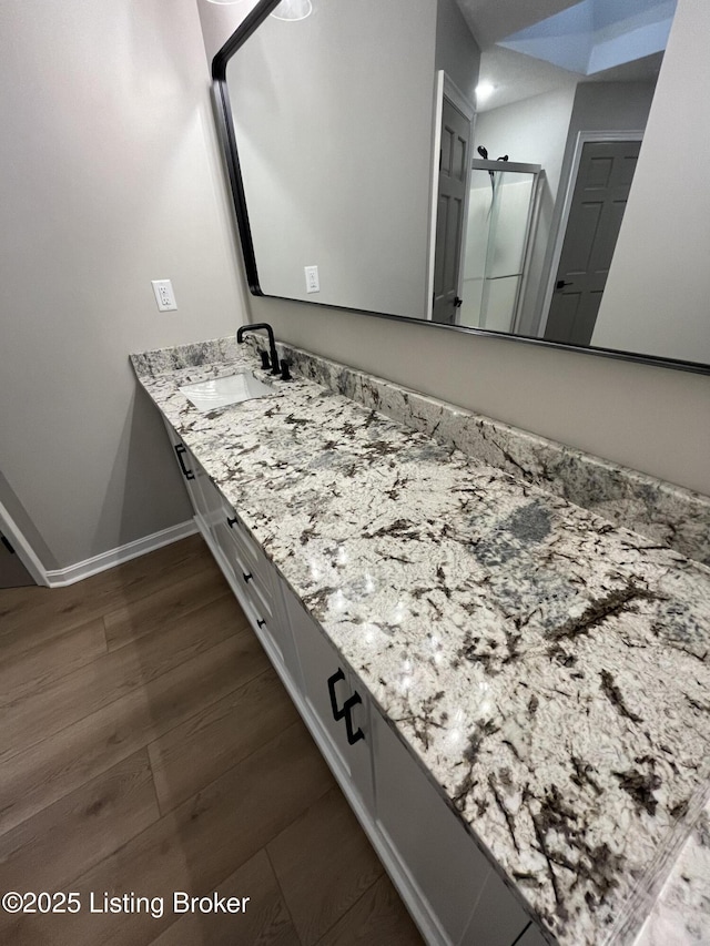 bathroom with a shower stall, vanity, baseboards, and wood finished floors