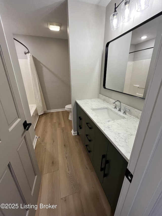 full bath featuring toilet, shower / bath combo with shower curtain, vanity, wood finished floors, and baseboards