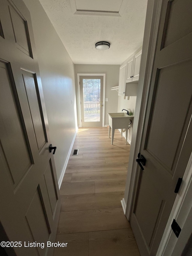 corridor featuring a textured ceiling, light wood finished floors, visible vents, and baseboards