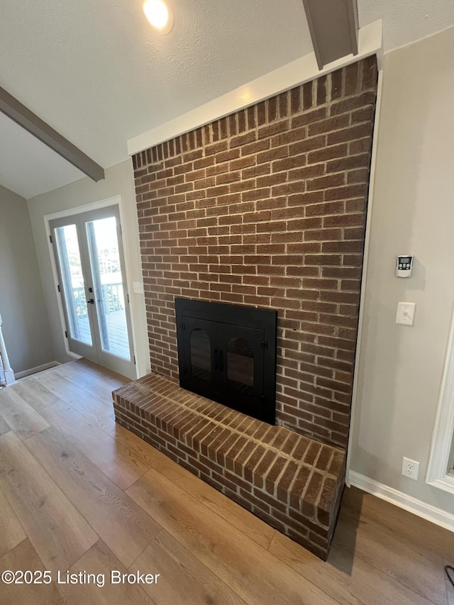 unfurnished living room featuring baseboards, beamed ceiling, wood finished floors, french doors, and a fireplace