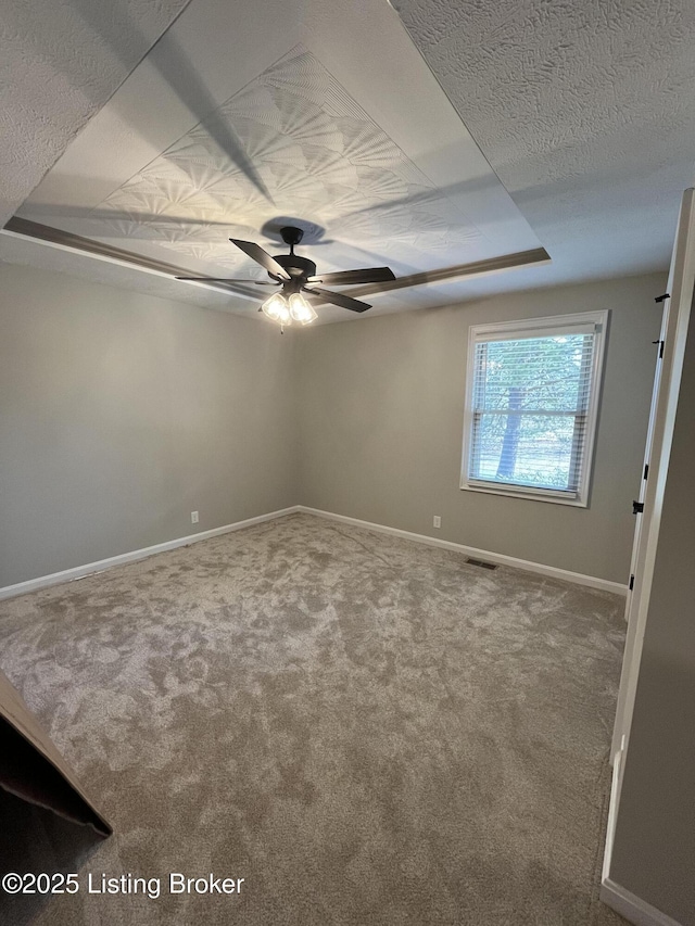 spare room with carpet floors, a tray ceiling, a ceiling fan, a textured ceiling, and baseboards