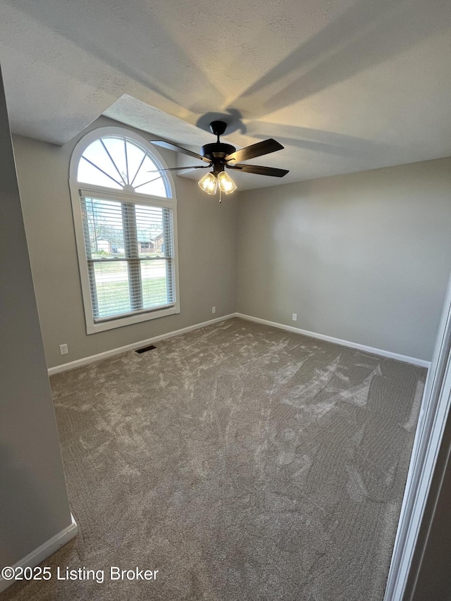 empty room with a textured ceiling, a ceiling fan, visible vents, baseboards, and carpet