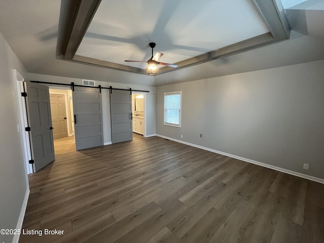 unfurnished bedroom with visible vents, a barn door, dark wood-type flooring, ensuite bath, and baseboards