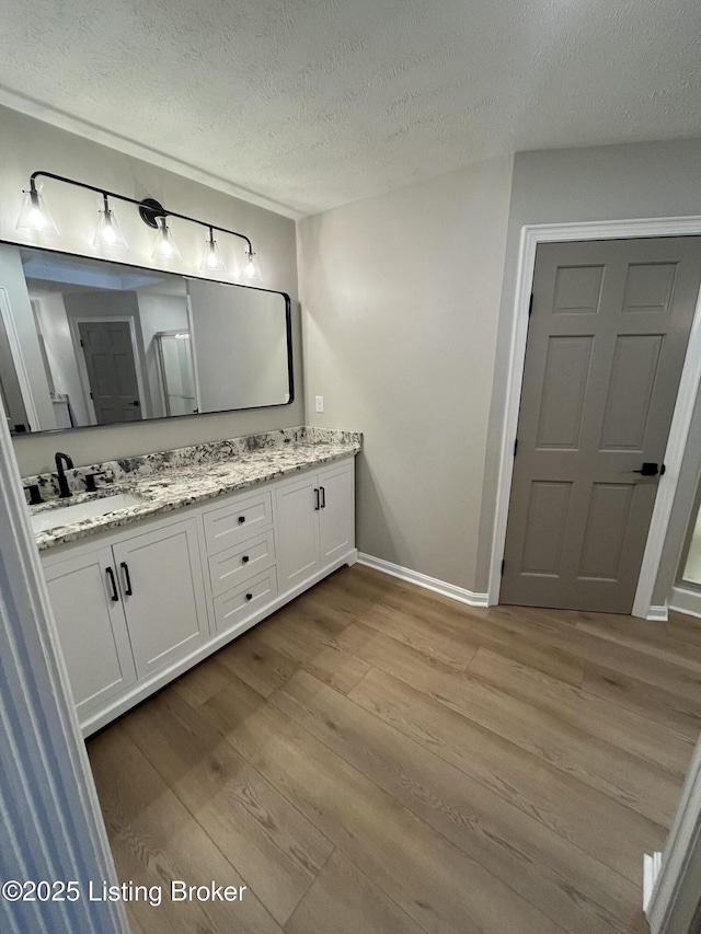 bathroom with double vanity, a sink, a textured ceiling, wood finished floors, and baseboards