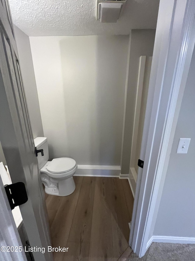 bathroom with baseboards, a textured ceiling, toilet, and wood finished floors