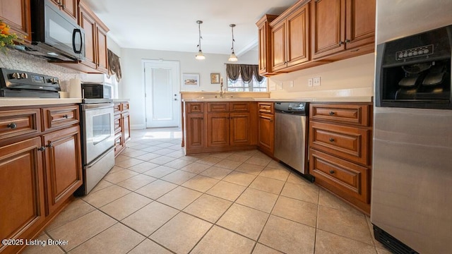 kitchen with a peninsula, a sink, light countertops, appliances with stainless steel finishes, and brown cabinetry