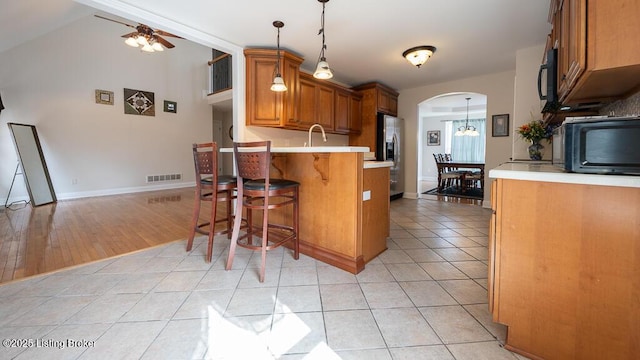 kitchen with arched walkways, black microwave, light tile patterned floors, visible vents, and stainless steel fridge