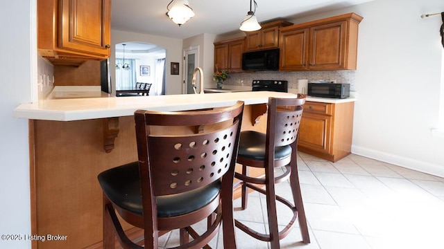 kitchen with black microwave, a kitchen breakfast bar, arched walkways, and brown cabinets