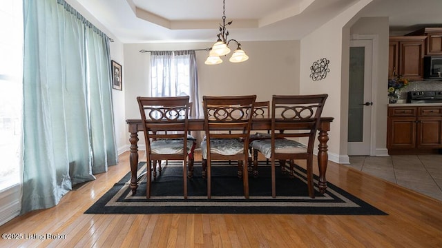 dining room with arched walkways, a raised ceiling, light wood-style flooring, and baseboards