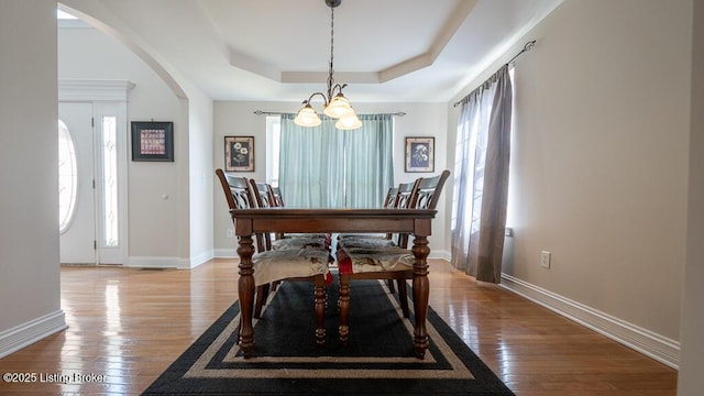 dining space with arched walkways, a raised ceiling, light wood-style flooring, and baseboards