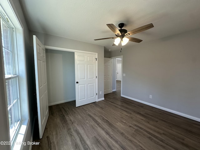 unfurnished bedroom featuring a closet, baseboards, dark wood finished floors, and a ceiling fan