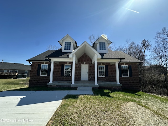 view of front of home with brick siding, a porch, a shingled roof, and a front lawn