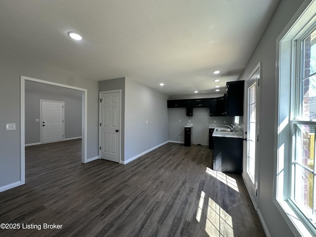 unfurnished living room with recessed lighting, baseboards, dark wood-type flooring, and a sink