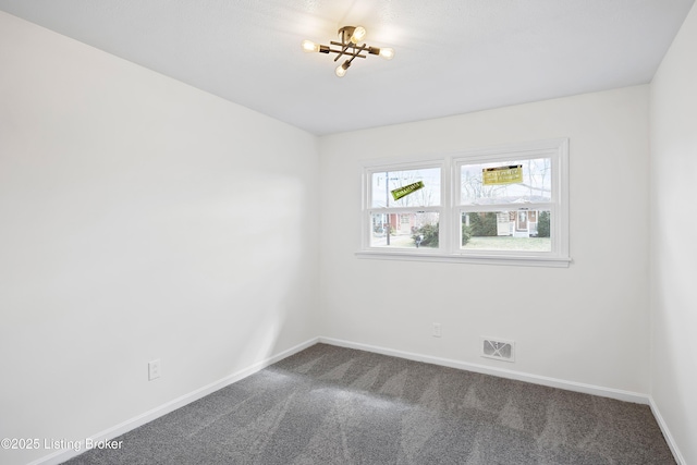 spare room with dark colored carpet, visible vents, and baseboards