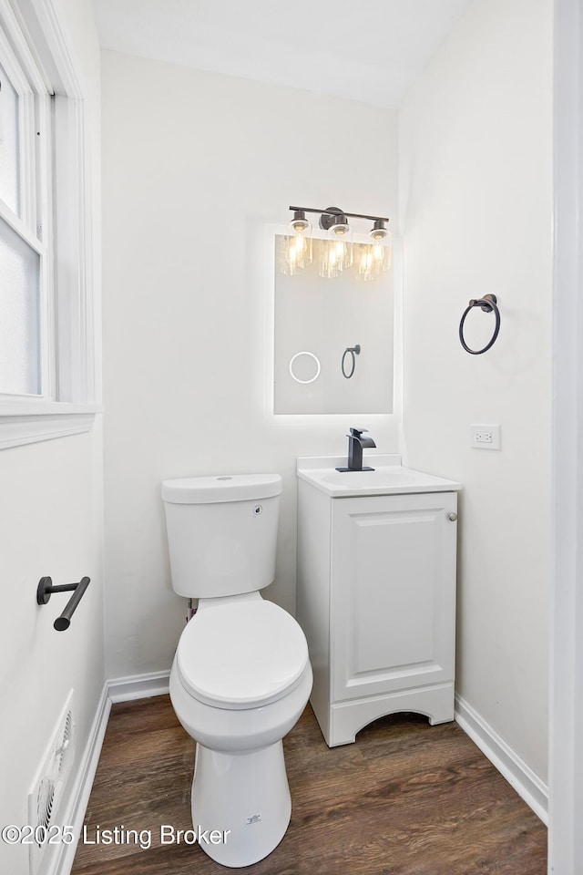 half bathroom with vanity, wood finished floors, toilet, and baseboards