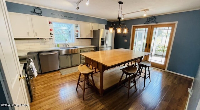 kitchen with wood finished floors, a sink, stainless steel appliances, white cabinetry, and backsplash