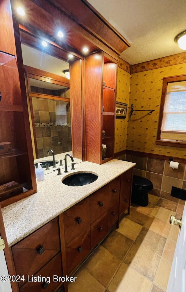 bathroom with a wainscoted wall, vanity, tile walls, tiled shower, and wallpapered walls