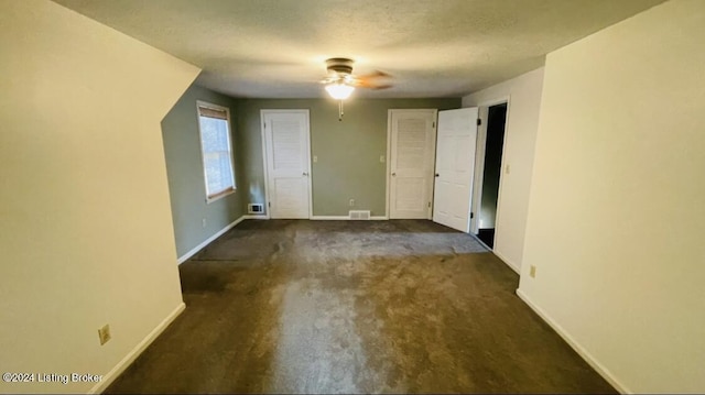 interior space with a textured ceiling, ceiling fan, carpet floors, visible vents, and baseboards