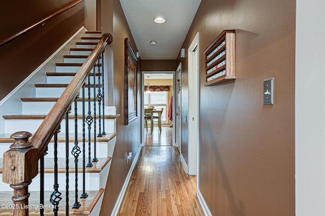 hall featuring a textured ceiling, baseboards, and wood finished floors