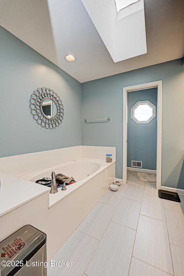 bathroom with a bath, a textured ceiling, visible vents, and baseboards