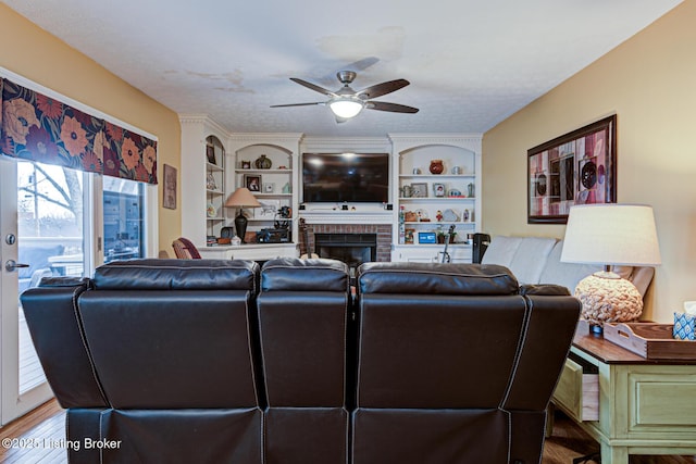 living room with a textured ceiling, built in shelves, a fireplace, wood finished floors, and a ceiling fan